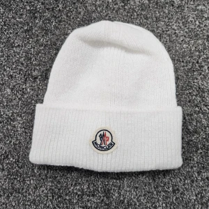 Vit stickad mössa från Moncler - Vit ribbstickad mössa från Moncler med uppvikt kant och klassisk Moncler-logga framtill. Enkel och stilren design som passar perfekt till kalla dagar. Tillverkad i mjukt stickat material för extra komfort.