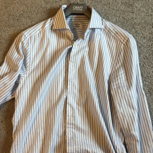 Randig skjorta Stenströms slimline 39 - Snygg vit skjorta från Stenströms med blåa ränder och slimline-passform. Tillverkad i exklusiv tvåfaldig bomull som känns lyxig mot huden. Klassisk krage, långa ärmar och knäppning framtill. Perfekt för dig som gillar stilrena och fräscha skjortor. Använd 1 gång