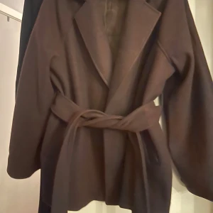 Brun kappa med bälte från Gina Tricot - Snygg brun kappa från Gina Tricot i storlek L. Jackan har breda slag, knyts med bälte i midjan och har långärmade ärmar. Perfekt för dig som gillar stilrena och klassiska plagg med en modern touch. Kappan är som ny har endast använts under två tillfällen. 