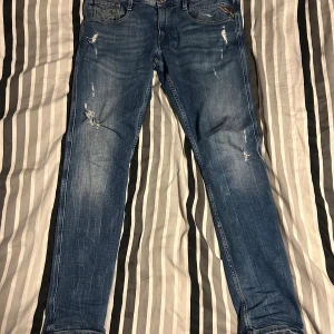 Replay jeans - Säljer ett par blå jeans från Replay med slitna detaljer och lätt tvättad look. Jeansen har klassisk femficksdesign, smal passform och är tillverkade i mjukt denimtyg. Perfekta för dig som gillar en avslappnad och trendig stil.