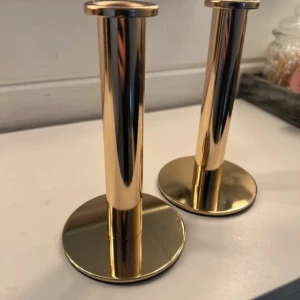 Ljusstakar guld - Två eleganta ljusstakar i polerad mässing med modern design. Passar perfekt som dekorativ detalj i hemmet. Ytan är blank och i mycket gott skick utan synligt slitage eller repor. Säljs som par och ger ett stilrent intryck i alla rum.