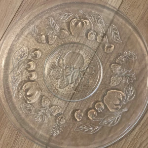 Glasfat med fruktmönster - Vackert glasfat med ingraverat fruktmönster, inklusive persikor, körsbär och jordgubbar. Perfekt för servering av kakor eller frukt. Fint skick utan synliga sprickor eller nagg. Elegant och dekorativ detalj till hemmet.