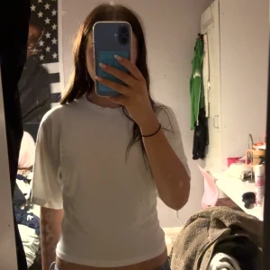 Vit basic t-shirt med kort ärm - Enkel och stilren vit t-shirt med korta ärmar och rund hals. Modellen är figurnära och passar perfekt till jeans eller shorts. T-shirten är gjord i mjuk bomull som känns skön mot huden.