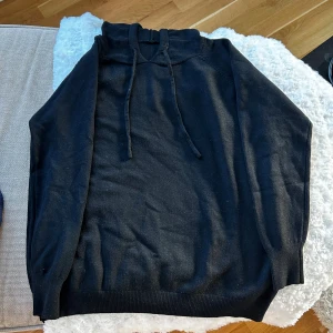 Svart hoodie med snörning - Svart hoodie med hög krage och snörning i halsen. Tröjan har en enkel och stilren design med ribbade muddar vid nederkant och ärmslut. Perfekt för dig som gillar en avslappnad och clean look.