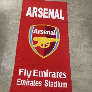 Röd Arsenal halsduk Emirates Stadium - Snygg röd halsduk med Arsenal-logga och texten 'Fly Emirates' samt 'Emirates Stadium' i vitt. Halsduken har en rektangulär form och är perfekt för dig som vill visa ditt stöd för Arsenal på matchen eller hemma. Tydliga färger och stort tryck gör den riktigt iögonfallande.