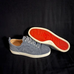 Ljusblå sneakers från Christian Louboutin - Snygga ljusblå sneakers från Christian Louboutin med klassisk röd sula och diskret logga på insidan. Skorna har rund tå, snörning och är tillverkade i mocka med beige skinnfoder. Perfekt för dig som vill ha en lyxig och stilren look. Låda lite tejpad.