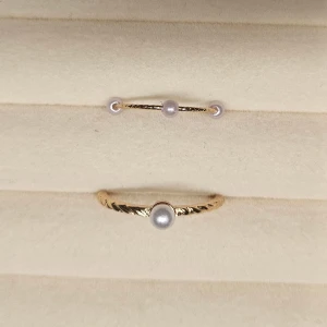 Två guldiga ringar med pärlor - Säljer två tunna guldiga ringar med vita pärlor. Den ena ringen har en enkel pärla i mitten och tvinnad design, medan den andra har tre små pärlor på rad. Perfekta för att stapla eller bära var för sig för en stilren look.