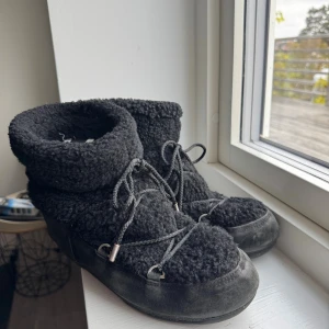 Svarta Moon Boot x YSL boots - Säljer ett par svarta Moon Boot boots med fluffig teddytextur och snörning framtill. Skorna har en robust sula och är perfekta för kalla dagar. Logga bak på hälen och på sulan. Riktigt mysiga och unika vinterboots!