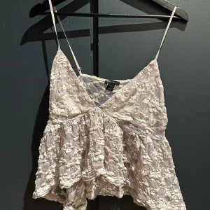 Vit blommig spetslinnetopp från Amisu - Supersöt vit linne-topp från Amisu i storlek XL. Toppen har tunna axelband, v-ringning och är täckt av blommig spets med volangdetaljer. Perfekt för dig som gillar romantisk och feminin stil. Materialet är spets med blommönster och toppen är lätt och luftig. Lite mindre i storleken, skulle säga M 