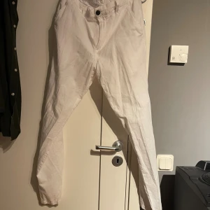 Vita tapered byxor från Jack & Jones - Snygga vita byxor från Jack & Jones med tapered passform. Byxorna har klassisk knapp och dragkedja framtill, två fickor bak med knappar och är tillverkade i bomull. Perfekta för dig som gillar stilrena och fräscha outfits.