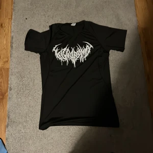 Svart compression gym tröja - Svart gym tröja sitter väldigt tight så du ser stor o stark ut i den o med korta ärmar och ett stort vitt tryck på bröstet i en cool, edgy stil. Materialet känns lätt och lite glansigt, perfekt för dig som gillar streetwear eller metal-vibe. Passformen är normal och trycket har en unik, nästan drip-effekt.