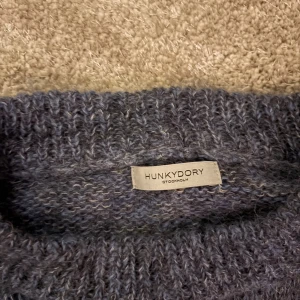 Mörkgrå stickad tröja Hunkydory - Säljer en mörkgrå stickad tröja från Hunkydory med rund hals och långa ärmar. Tröjan har en mjuk och fluffig känsla, perfekt för kyliga dagar. Ribbstickade muddar vid ärmslut och nederkant ger en snygg passform. Enkel och stilren design.
