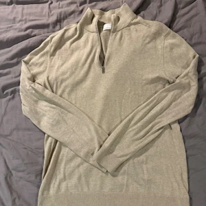 Beige half zip tröja Selected Homme storlek L - Snygg beige långärmad tröja från Selected Homme med half zip och hög krage. Tröjan är stickad i mjuk bomull och har ribbade muddar vid ärmslut och nederkant. Perfekt för dig som gillar stilrena och enkla plagg. Sömmarna i armhålorna är lite dåliga där av priset, men annars är tröjan väldigt fin. Ny pris ca 700kr