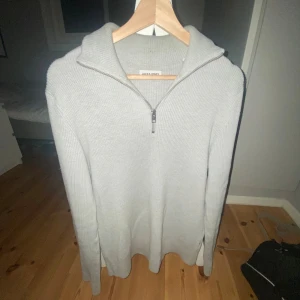Ljusgrå stickad half zip från Jack & Jones - Säljer en ljusgrå stickad tröja från Jack & Jones i storlek M. Tröjan har en snygg half zip-dragkedja vid halsen och ribbad struktur. Perfekt för dig som gillar stilrena och bekväma plagg med lång ärm och avslappnad passform.