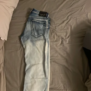 Ljusblå slitna jeans från replay - Säljer ett par ljusblå jeans från replay med slitningar och distressed detaljer framtill. Jeansen har klassisk femficksdesign, normal passform och är tillverkade i bomull. Perfekt för dig som gillar en avslappnad och trendig look.