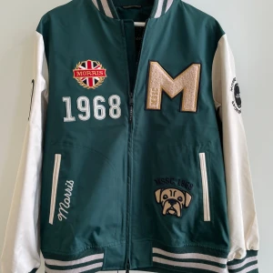 Morris bomberjacka - Helt ny, lappen hänger kvar! Snygg bomberjacka från Morris i grönt och vitt med broderade patches. Jackan har randiga muddar, dragkedja och coola detaljer på ärmarna. Perfekt för dig som vill sticka ut med sportig stil. Passar dig som är ca 175 cm lång. 