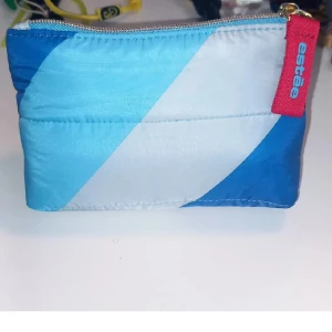 Blå-vit necessär från Estée Lauder - Necessär från Estée Lauder i coolt blått och vitt med snedrandigt mönster. Väskan har dragkedja med röd etikett och är tillverkad i syntetmaterial. Perfekt storlek för smink eller hudvård, och har en mjuk, quiltad känsla. Innehåller fyra miniprodukter: en 30ml Perfectly Clean rengöring, en 7ml DayWear ansiktskräm med SPF och Advanced Night Repair serum (7ml)/kräm (5ml). Perfekt för dig som vill testa mini versioner av produkten innan du köper den större.