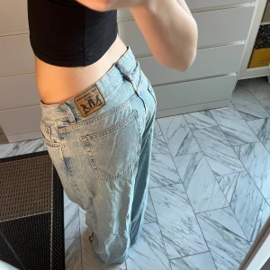 Baggy ljusblå jeans Sweet Skateboarding - Baggy ljusblå jeans från Sweet Skateboarding Company med klassisk femficksdesign och bred passform. Jeansen har låg midja, raka ben och är tillverkade i slitstarkt bomullsjeans. Perfekta för en avslappnad streetstil.