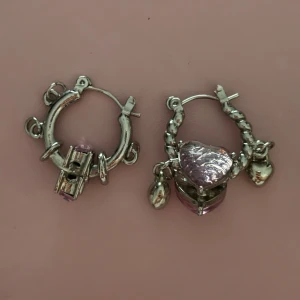 Silvriga örhängen med lila hjärtan - Chunky silvriga hoops med detaljerade hängen, bland annat lila hjärtformade berlocker och små silvriga hjärtan. 