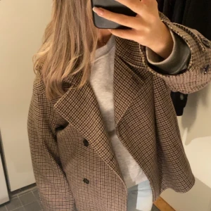 Rutig ullrock från Arket, strl 36 - Säljer en snygg rutig kappa från Arket i storlek 36. Jackan är i brunt och beige med bred krage, dubbelknäppning och tillverkad i italiensk ull. Använd fåtal gånger!!