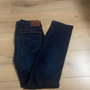 Mörkblå Lee Rider jeans W34 L32 - Säljer ett par mörkblå Lee Rider jeans i klassisk straight fit. Jeansen har snygga kontrastsömmar, läderpatch med Lee-logga och femficksdesign. Tillverkade i slitstarkt denimtyg som ger en tidlös look.