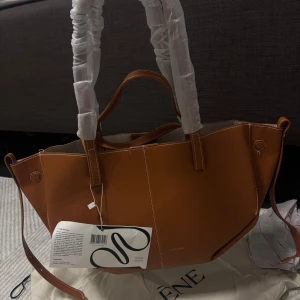 Brun handväska Polène inspirerad  - Snygg handväska i brunt/orange skinn med stilren design och guldfärgad logga. Väskan har både handtag och axelrem, samt en praktisk innerficka med dragkedja. Helt ny!🩷 Cyme Mini modellen😊Färgen är mer som bild nummer 2-4!!!