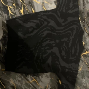 Svart stickad polotröja med mönster - Säljer en svart stickad polotröja med mörkgrått abstrakt mönster. Tröjan har ribbade muddar och hög krage som ger en cool vibe. Perfekt för dig som gillar streetstyle och vill ha något unikt i garderoben.