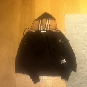 Svart Burberry hoodie med rutig huva - Svart hoodie från Burberry. Den är för liten för mig så jag säljer den. Den är oanvänd och i bra skick. Skriv om minsta lilla fråga. PRIS KAN DISKUTERAS. Den S-Xs