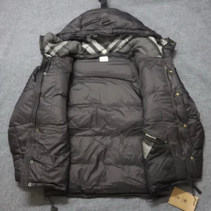 Svart dunjacka från Burberry - Säljer en svart dunjacka från Burberry med klassisk logotyp på ärmen och rutigt foder i grått och vitt. Jackan har huva, dragkedja och knappar framtill samt praktiska fickor. Perfekt för kalla dagar med sin quiltade design och varma material.