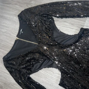 Klänning - Svart kort paljettklänning från Fashion Nova med lång ärm, v-ringning och cut-out midja. Storlek S. Klänningen har dragkedja i ryggen och en figurnära passform. Använd en gång och i utmärkt skick 🖤