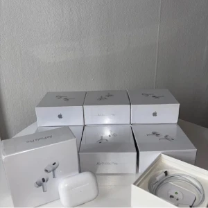 AirPods Pro - Apple AirPods Pro med aktiv brusreducering och trådlös laddningsetui. Flera enheter i originalförpackning, komplett med laddningskabel. Hörlurarna och etuierna ser ut att vara i gott skick, med endast mindre tecken på normalt bruk. Perfekt för musik, samtal och träning.