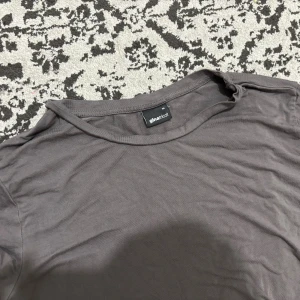 Mörkgrå t-shirt från Gina Tricot - En basic mörkgrå t-shirt från Gina Tricot i mjuk bomull. Klassisk rund halsringning och korta ärmar. Perfekt att matcha med jeans eller kjol för en enkel och clean look.