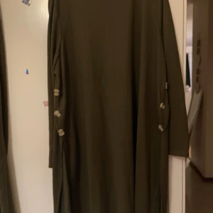 Olivgröna loose byxor med knappar - Säljer ett par olivgröna byxor med loose passform och vida ben. Byxorna har dekorativa knappar längs sidorna och är gjorda i ett mjukt, tunt material som känns skönt mot huden. Perfekt för dig som gillar avslappnad stil och vill ha något bekvämt.