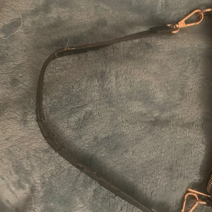 Svart axelväska med krokopräglad yta - Snygg svart axelväska med krokopräglad yta och guldfärgade detaljer. Väskan har en avtagbar axelrem och dragkedja upptill. Perfekt storlek för det viktigaste och ger en cool vibe till din outfit.