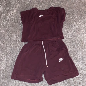 Vinröda Nike shorts med snörning - Säljer ett par vinröda Nike shorts i mjuk bomull med vit snörning i midjan och klassisk Nike-logga tryckt på benet. Modellen är loose fit och har elastisk midja för extra komfort. Perfekta för chill dagar eller träning.