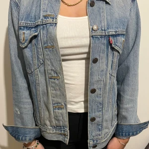 Levi's ljusblå jeansjacka - Säljer en klassisk ljusblå jeansjacka från Levi's med bruna knappar och två bröstfickor med lock. Jackan har en loose passform och är tillverkad i slitstarkt denim. Perfekt att slänga över en t-shirt för en chill look. Väldigt fin washed out modell. 