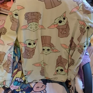 Baby Yoda mjukisbyxor med tryck samt tröja  - Supermysiga mjukisbyxor med all-over Baby Yoda-tryck från Star Wars. Byxorna är ljusgröna med söta motiv i grönt, rosa och brunt. Perfekta för chill eller gamingkvällar. Mjukt och stretchigt material för extra komfort.