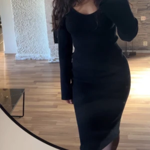 Svart ribbad långärmad klänning - Säljer en svart, ribbad klänning med lång ärm och figurnära passform. Klänningen har en rundad urringning och är i midi-längd, perfekt för dig som gillar en stilren och enkel look. Materialet är stretchigt och bekvämt.