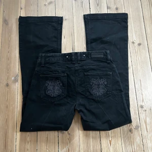 Svarta bootcut jeans Jasper Conran - Svarta bootcut jeans från Jasper Conran med snygg broderad detalj på bakfickorna. Klassisk femficksmodell med rosa sömmar på insidan av linningen. Jeansen har normal passform och är tillverkade i ett mjukt bomullstyg.