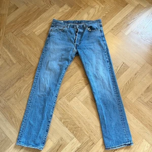 Levi's 501 ljusblå jeans straight fit w34 L32 - Klassiska Levi's 501 jeans i ljusblå tvätt med raka ben och femficksmodell. Jeansen har knappgylf och är tillverkade i slitstark bomullsdenim. Perfekt för dig som gillar en tidlös och avslappnad look. Hör av er vid frågor