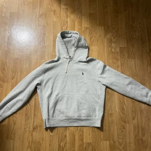 Grå hoodie från Polo Ralph Lauren - Säljer en väldigt fin, inte använd (fel storlek) stilren grå hoodie från Polo Ralph Lauren med klassisk broderad logga på bröstet. Tröjan har huva med snörning, magficka och är tillverkad i mjuk bomullsmix. 
