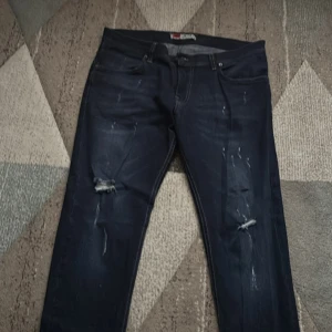 Mörkblå Replay jeans med slitningar - Säljer ett par mörkblå jeans från Replay med snygga slitningar och hål på knäna. Klassisk femficksmodell med raka ben och normal passform. Perfekta för dig som gillar en avslappnad och trendig look.