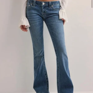 Blå bootcut jeans från True Religion - Säljer ett par blå jeans från True Religion med klassiska kontrastsömmar och ikoniska bakfickor. Modellen har bootcut-ben och lågmidjade. Jeansen är tillverkade i denim med lätt tvättad look och har knapp- och dragkedjestängning framtill.