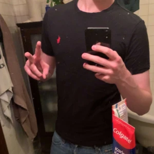 Svart t-shirt från Polo Ralph Lauren - Svart t-shirt från Polo Ralph Lauren med klassisk rund hals och röd broderad logga på bröstet. Modellen är custom slim fit och tillverkad i mjuk bomull som känns skön mot huden. Perfekt för dig som gillar stilrena och enkla plagg med en touch av lyx.