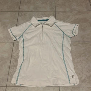 Vit sportig kortärmad skjorta från Röhnisch - Vit sporttröja från Röhnisch med turkosa sömmar och halv dragkedja framtill. Köpt second hand. 