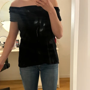 Svart topp med detalj - Svart ärmlös topp med snygg draperad krage som kan bäras både på axlarna och offshoulder.