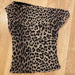 Leopardmönstrad oneshoulder topp Gina Tricot - Säljer en snygg leopardmönstrad topp från Gina Tricot i storlek XS. Modellen är oneshoulder och har en tight passform. Färgen är beige med svarta leopardfläckar. Materialet är lätt och stretchigt, perfekt för att sticka ut med en cool vibe. Aldrig använt köpte föra året höst ny pris 299