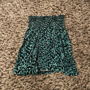 Turkos mönstrad kortkjol med smock - Snygg kortkjol med turkos och svart camouflage-mönster. Kjolen har ett brett och stretchigt midjeband som ger en skön och flexibel passform. Materialet är mjukt och lätt, perfekt för varmare dagar. Passar dig som gillar att sticka ut med coola mönster och färger.💗Vet ej storlek då lappen i kjolen är borta men passar ca XS-M