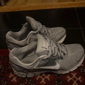Grå Nike sneakers med mesh - Säljer ett par grå Nike sneakers med cool mesh-överdel och klassisk vit swoosh på sidan. Skorna har snörning och en chunky sula som ger skön streetkänsla. Perfekta för dig som gillar sportig stil och vill ha något som sticker ut.