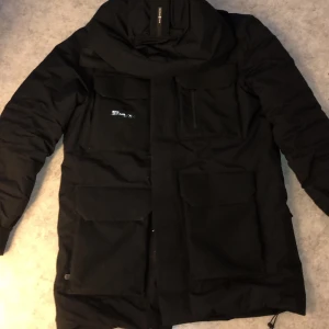 Sail racing GLACIER BAY PARKA  - Sail Racing Glacier Bay Parka är en slitstark och bekväm vinterparkas i modern design och medellång längd tillverkad i Gore-Tex Infinium med Gore-Tex stretchtyg över axlar, ärmar och huva som båda ger ett vindätt och vattenavvisande material med god andningsförmåga samt fyllning av dun- och fjäderblandning